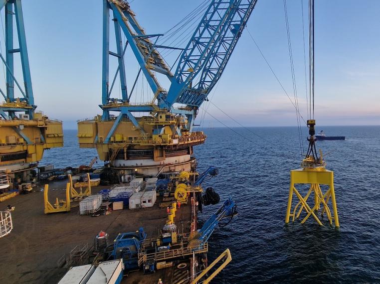 Yellow structure being listed into the sea by a large crane