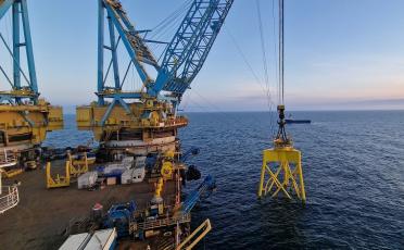 Yellow foundation for offshore wind turbine being lifted into the sea by large crane