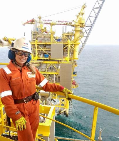 Woman standing in orange overalls with yellow oil platform in background